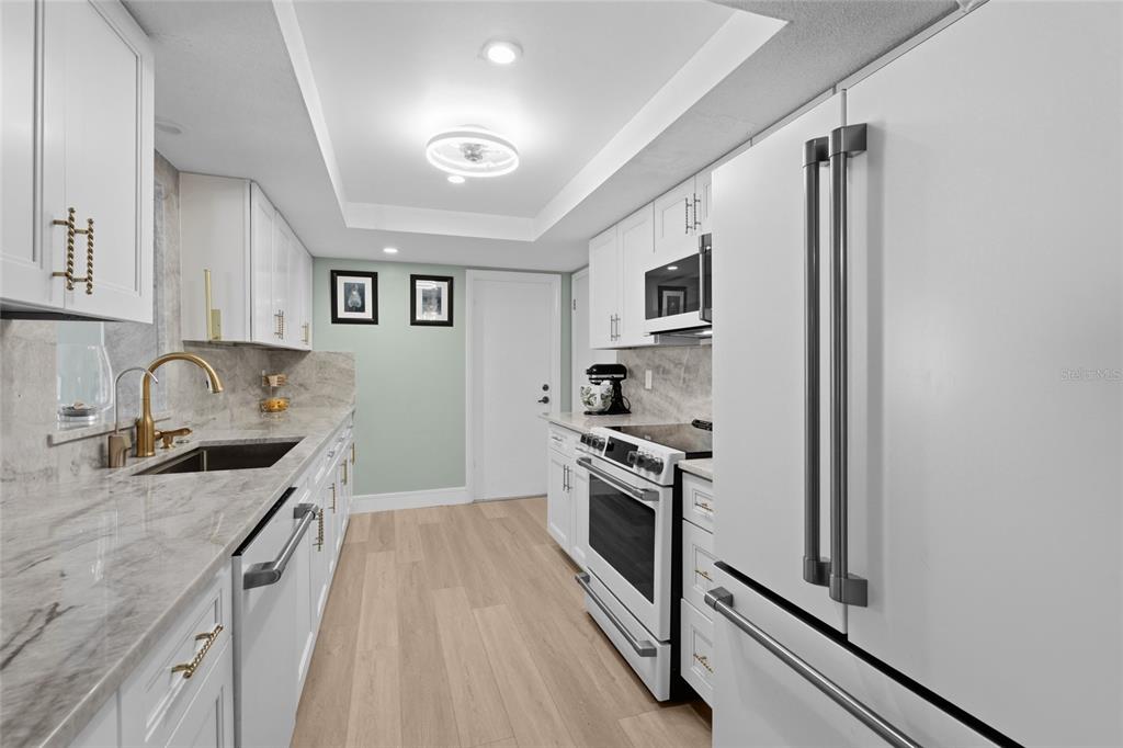 A galley kitchen features white cabinets, marble-look countertops, stainless steel appliances, and light wood flooring — 3274 SAVAGE ROAD, SARASOTA, FL