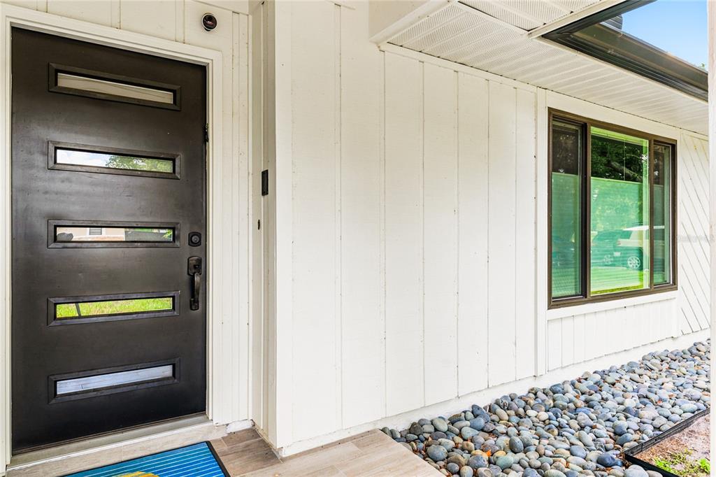 A modern dark front door with horizontal windows sits next to white vertical siding — 4039 COOL WATER COURT, WINTER PARK, FL