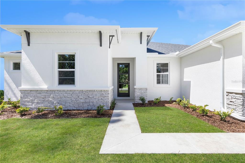 A modern white stucco house features a stone veneer base and a glass-paneled front door — 13 SW 34TH PLACE, CAPE CORAL, FL
