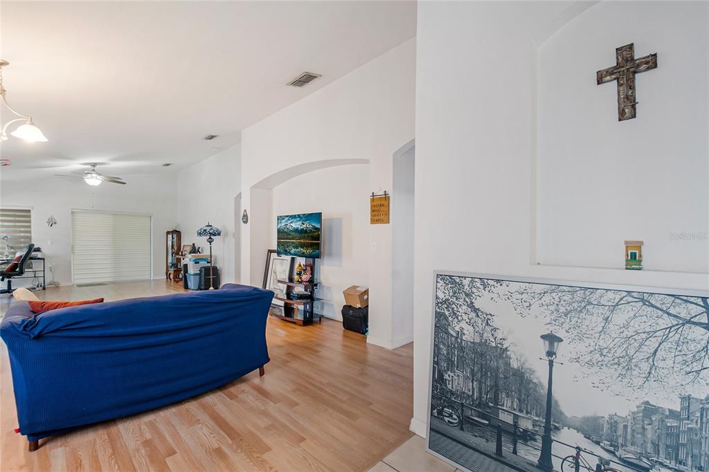A living room features light wood flooring, a blue sofa, and a wall-mounted cross — 172 ACADIA DRIVE, KISSIMMEE, FL