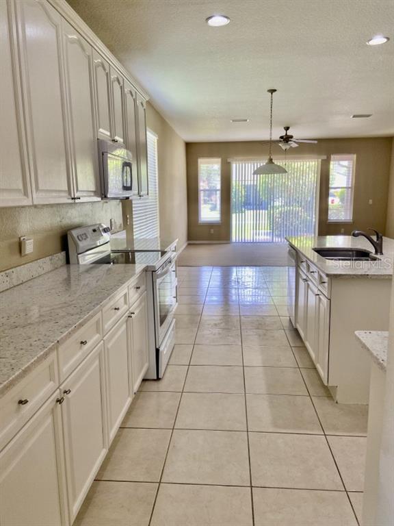 A kitchen with white cabinets, granite countertops, and tile flooring leads to a living area — 6679 DUNCASTER STREET, WINDERMERE, FL