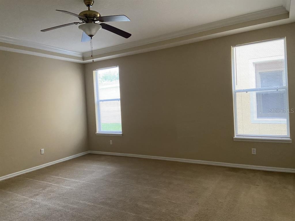An empty bedroom features beige walls, tan carpeting, a ceiling fan, and two windows — 6679 DUNCASTER STREET, WINDERMERE, FL