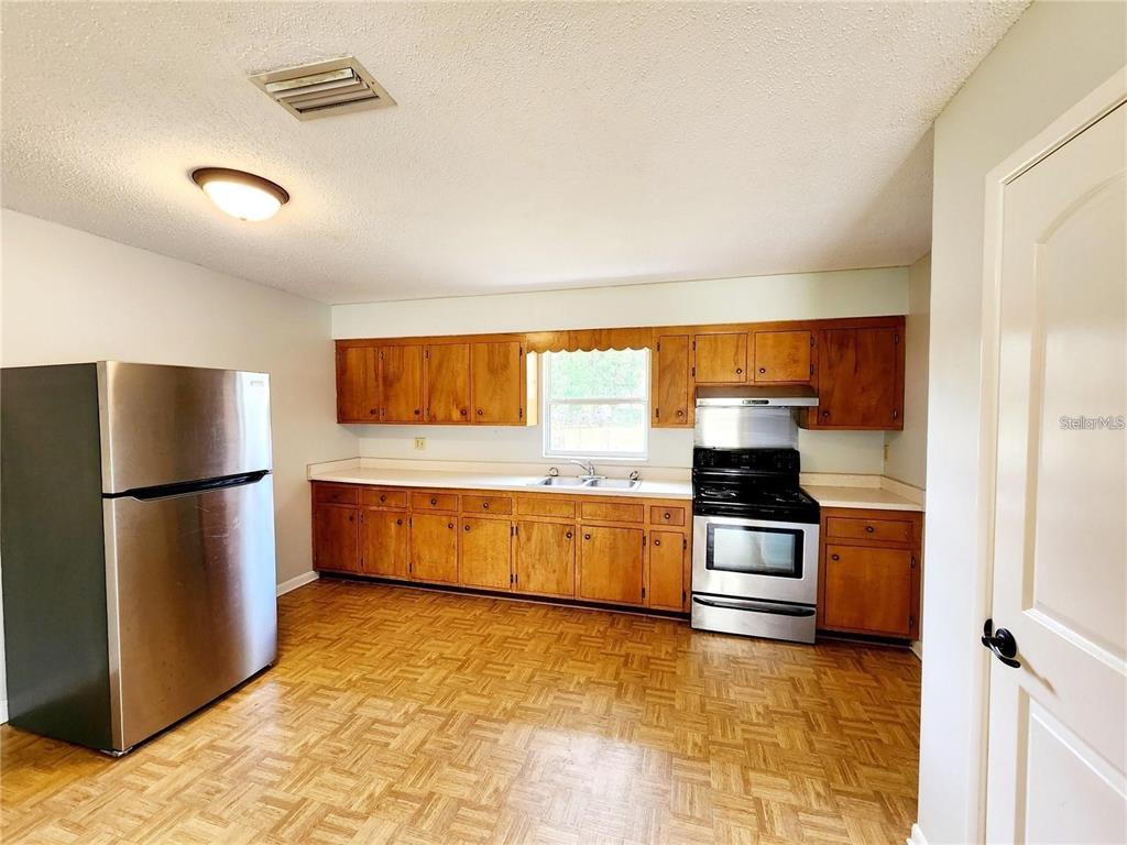 A kitchen features wood cabinets, stainless steel appliances, and a parquet wood floor — 420 N COURT STREET, BRONSON, FL