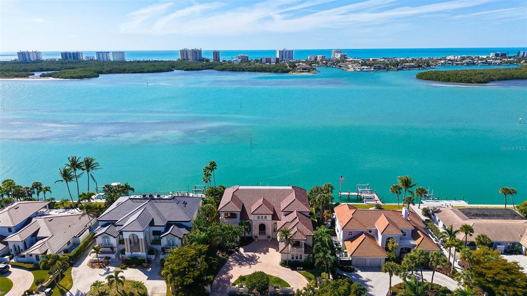 An aerial view shows waterfront homes with tiled roofs along a bay under a blue sky — 570 S SPOONBILL DRIVE, SARASOTA, FL