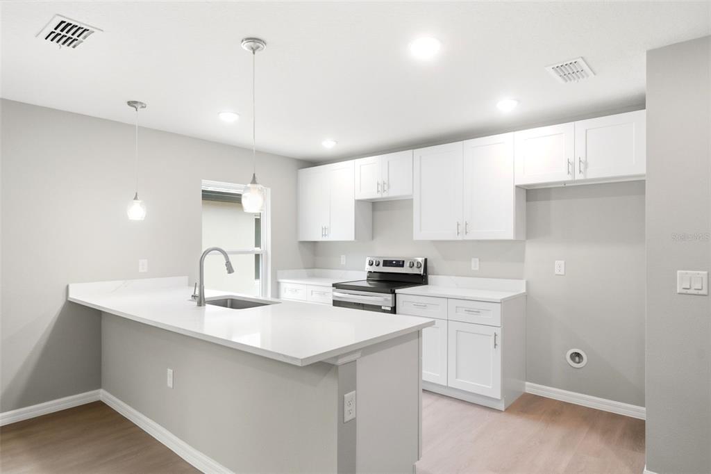 A modern kitchen features white cabinetry, quartz countertops, a kitchen island, and stainless steel appliances — 2107 SUANEE AVENUE UNIT 200, EUSTIS, FL