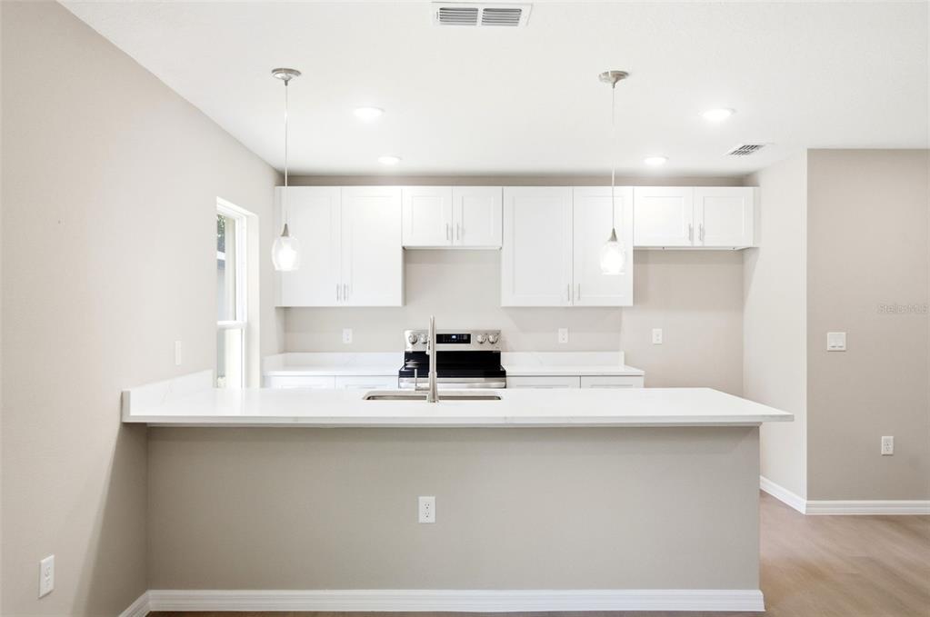 A kitchen features white cabinets, a white quartz countertop, and a breakfast bar — 2107 SUANEE AVENUE UNIT 200, EUSTIS, FL
