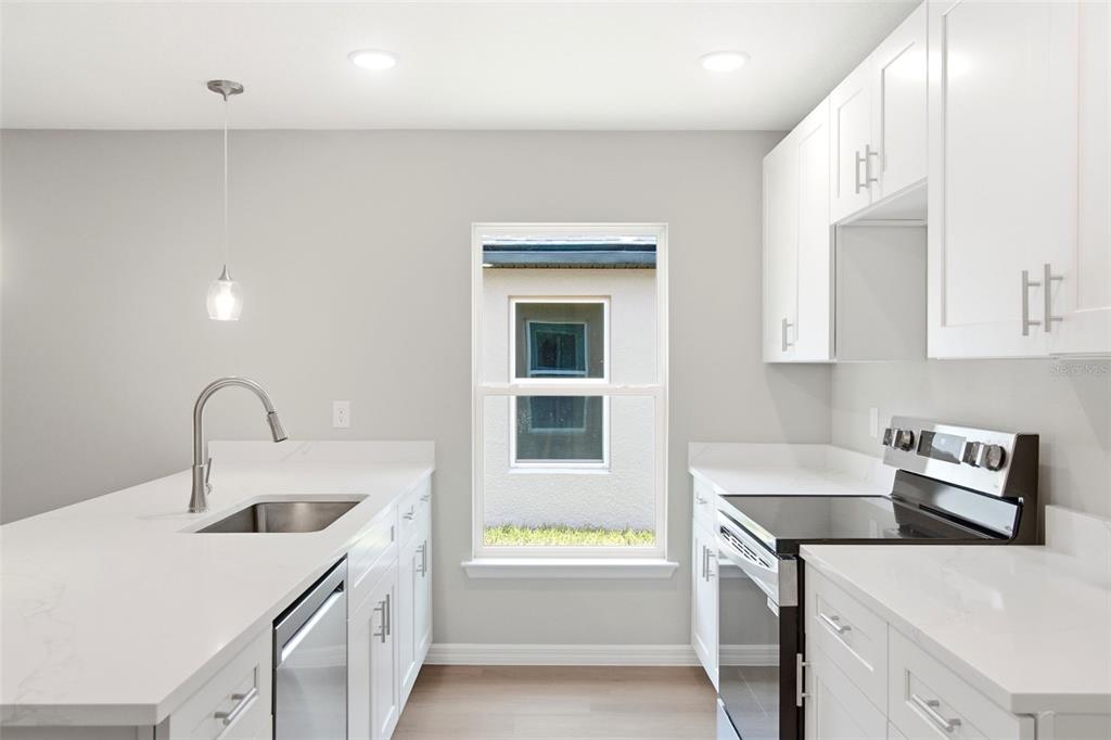 A modern kitchen features white cabinets, quartz countertops, a stainless steel sink, and a window — 2107 SUANEE AVENUE UNIT 200, EUSTIS, FL