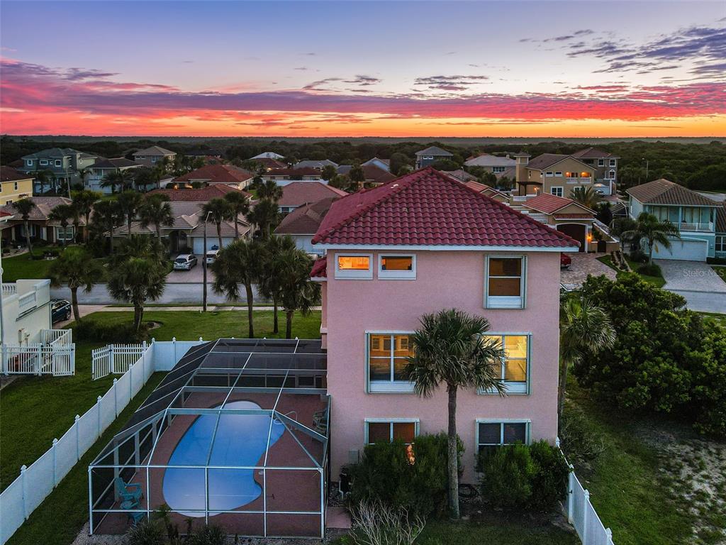 An aerial view of a three-story pink house with a screened-in pool at sunset — 3817 ISLAMORADA DRIVE, ORMOND BEACH, FL