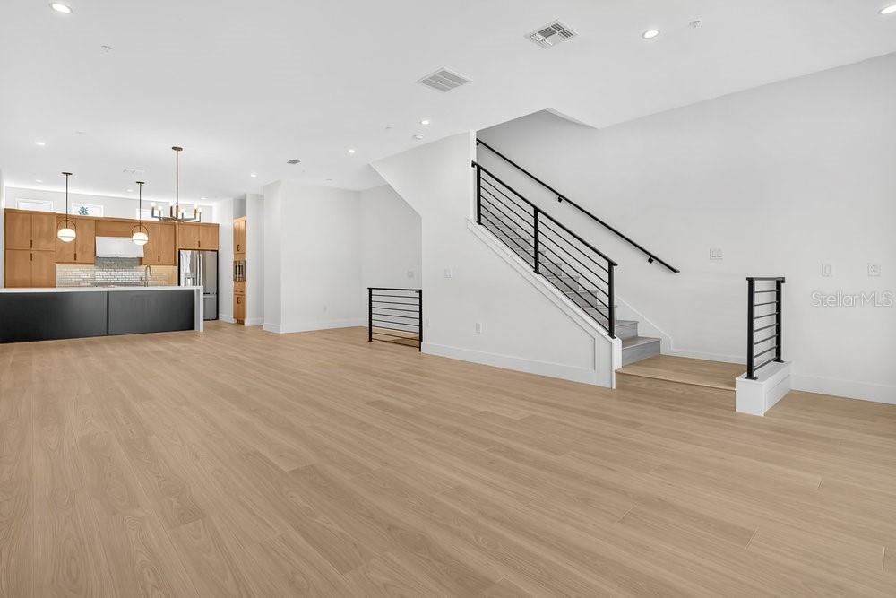 An open-concept living area features light wood flooring, a modern staircase, and a kitchen — 1008 E ROBINSON, ORLANDO, FL
