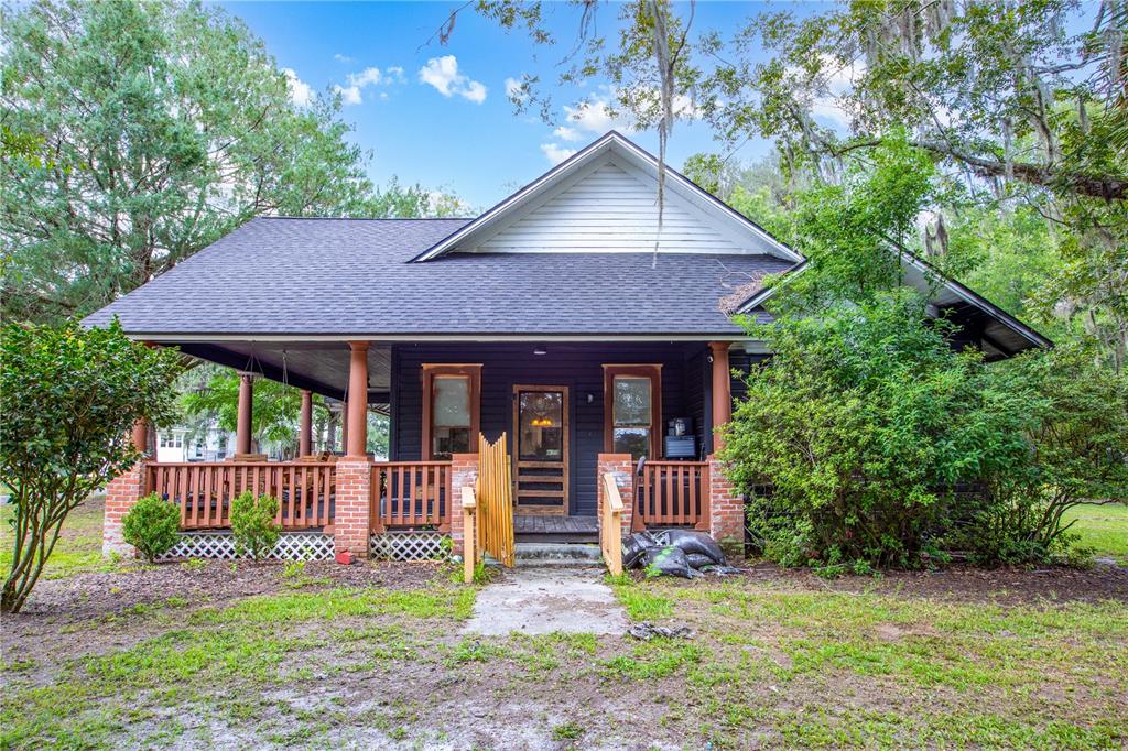 A dark-sided house with a large front porch, brick pillars, and a gabled roof — 13328 NE 230TH COURT, RAIFORD, FL