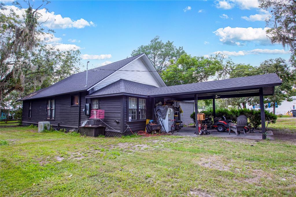The exterior of a dark-painted house features a side carport and a grassy yard — 13328 NE 230TH COURT, RAIFORD, FL