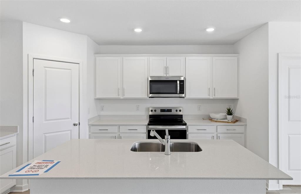 A modern kitchen features white cabinets, stainless steel appliances, and a large central island — 12809 BLUE REFLECTION AVENUE, PARRISH, FL