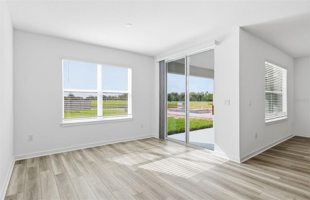 A bright, empty room with light wood-look flooring, white walls, large windows, and sliding doors — 12809 BLUE REFLECTION AVENUE, PARRISH, FL