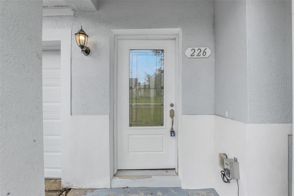 A white front door with a decorative glass insert sits in a room with wood-look flooring — 226 HAVERSHAM ROAD, DELTONA, FL