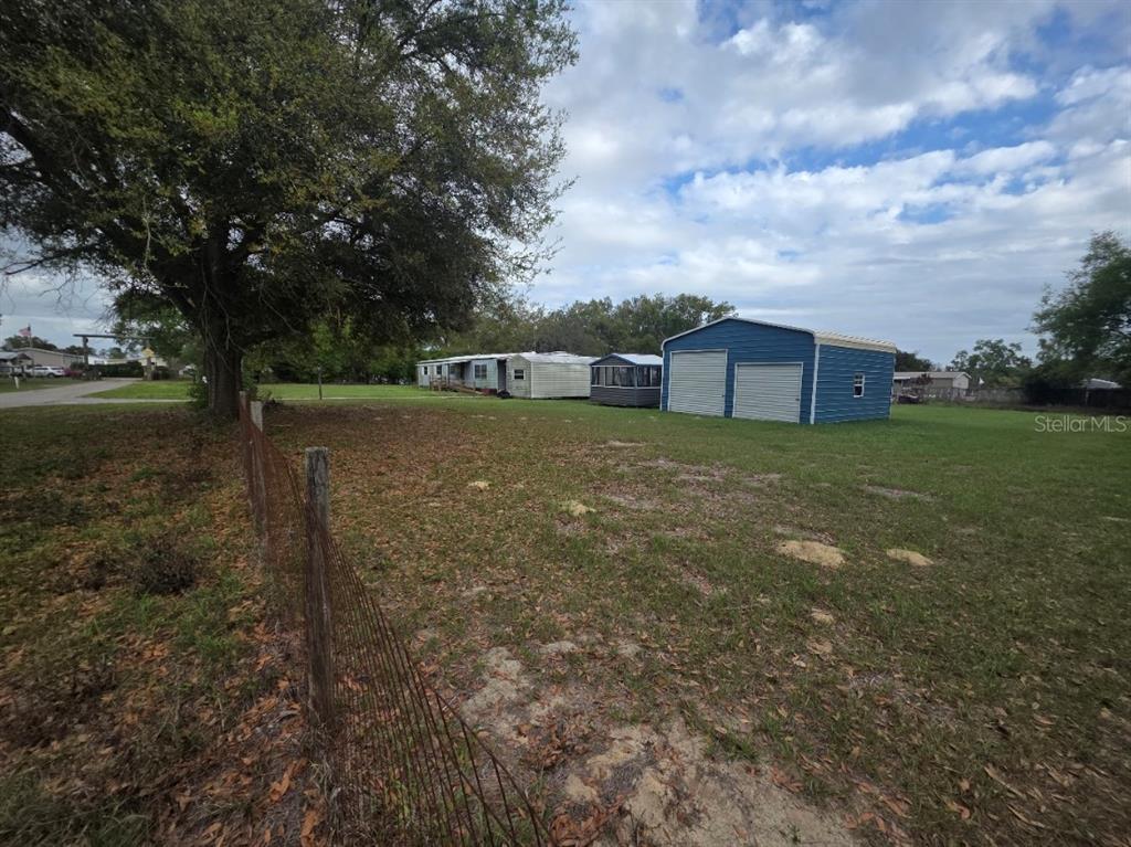 A grassy lot features a wire fence, a large tree, a mobile home, and a garage — 37414 NORTHSIDE DRIVE, ZEPHYRHILLS, FL