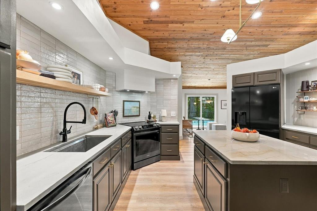 A modern kitchen features dark cabinets, light countertops, a wood-plank ceiling, and a black refrigerator — 1515 MIDNIGHT PASS WAY, CLEARWATER, FL