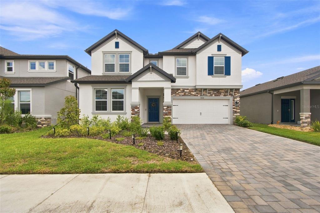 A two-story suburban house features a stone-accented facade, a two-car garage, and a paved driveway — 31840 SAPNA CHIME DRIVE, WESLEY CHAPEL, FL