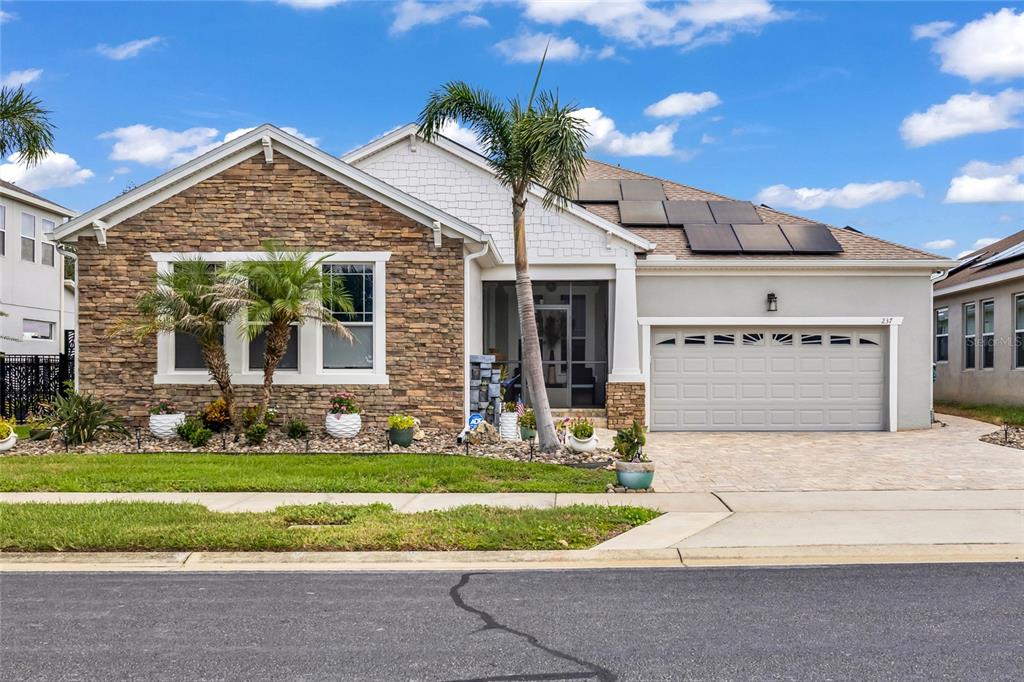 A single-story house with stone veneer, white siding, a paved driveway, and rooftop solar panels — 237 BLUE CYPRESS DRIVE, GROVELAND, FL