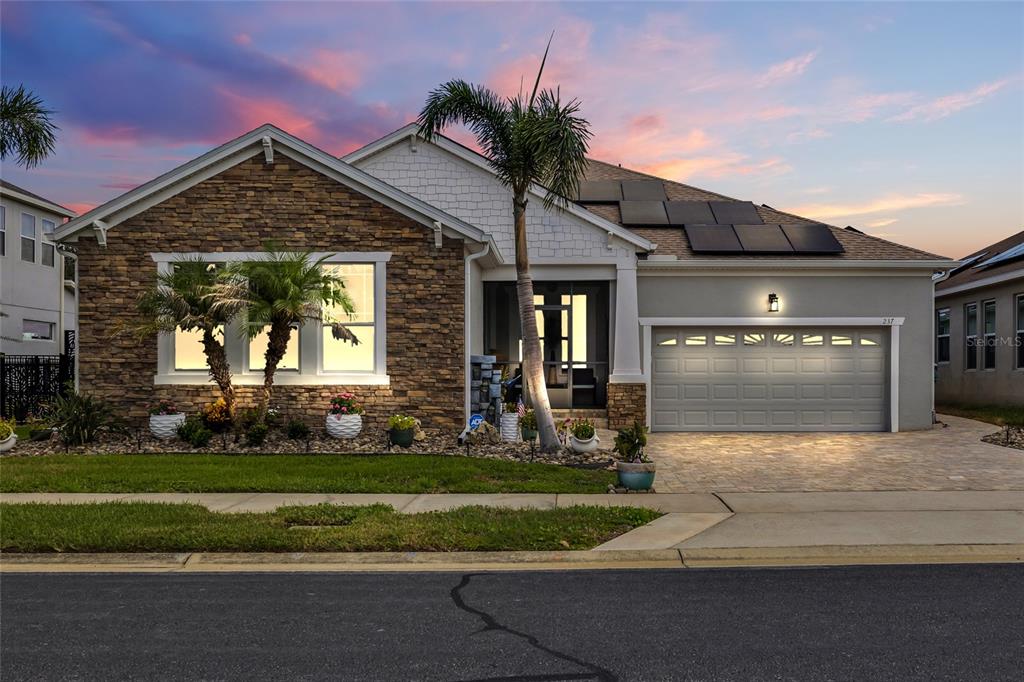 A single-story house with stone veneer, white siding, solar panels, and a paved driveway at sunset — 237 BLUE CYPRESS DRIVE, GROVELAND, FL