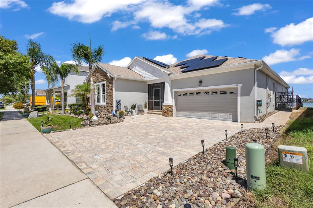 A single-story house with a stone facade, a paved driveway, and solar panels on the roof — 237 BLUE CYPRESS DRIVE, GROVELAND, FL