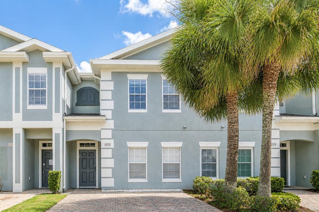 A two-story townhouse exterior with light blue stucco, white trim, and a paved driveway — 2376 CARAVELLE CIRCLE, KISSIMMEE, FL