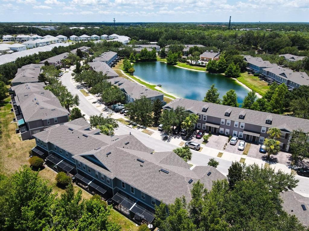 An aerial view shows multiple multi-story townhome buildings surrounding a central pond and parking areas — 2376 CARAVELLE CIRCLE, KISSIMMEE, FL