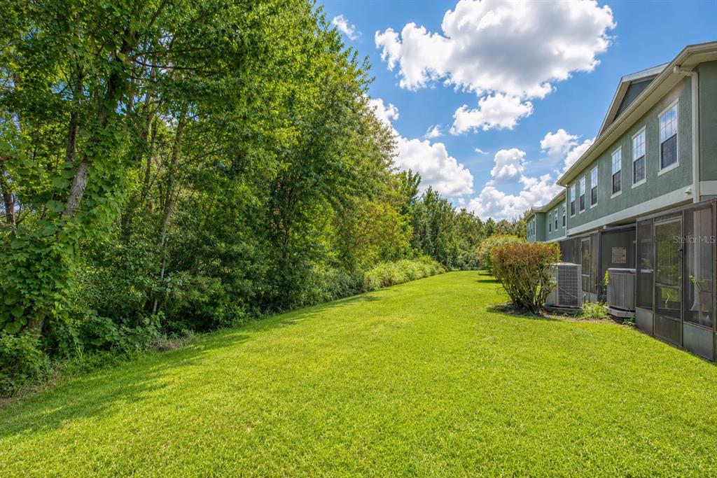 A grassy yard sits beside a multi-story residential building with screened-in patios and dense trees — 2376 CARAVELLE CIRCLE, KISSIMMEE, FL