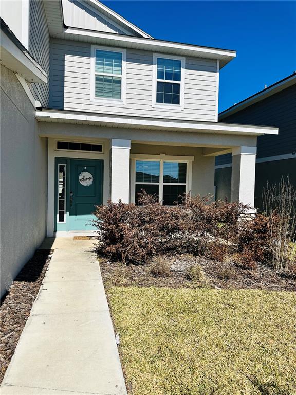 A light-colored two-story house features a covered front porch, a teal door, and landscaping — 36097 WELSH GLADE ROAD, DADE CITY, FL