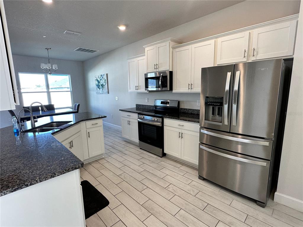 A kitchen features white cabinets, stainless steel appliances, granite countertops, and light wood-look tile flooring — 36097 WELSH GLADE ROAD, DADE CITY, FL