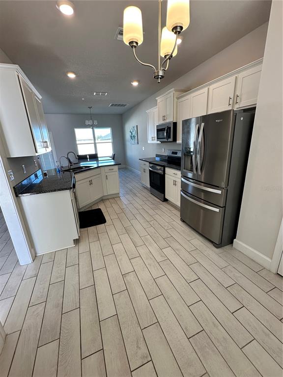 A kitchen features white cabinets, stainless steel appliances, dark countertops, and light wood-look tile flooring — 36097 WELSH GLADE ROAD, DADE CITY, FL