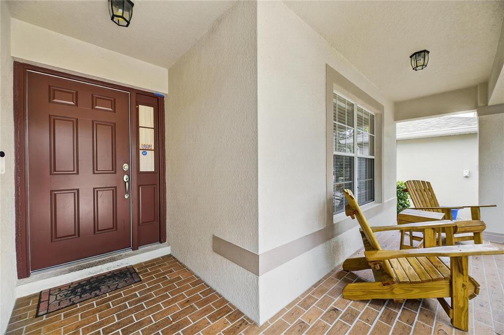 A covered front porch features brick flooring, a reddish-brown door, and two wooden chairs — 424 DOWN PINE DRIVE, SEFFNER, FL