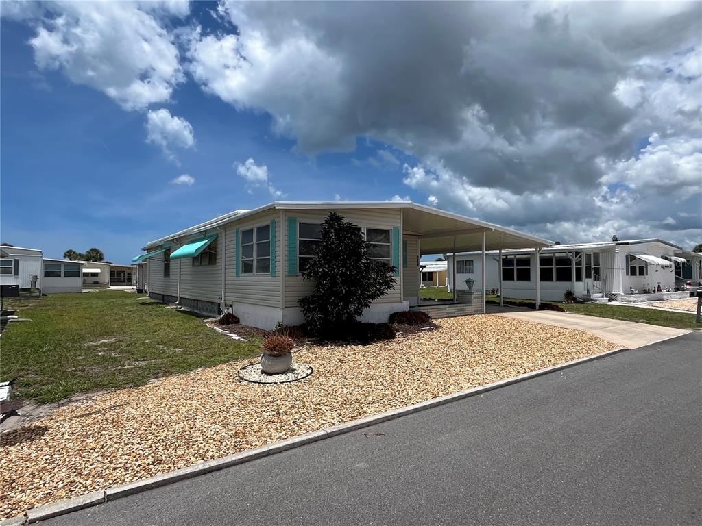 A single-story manufactured home with a carport, light siding, and a gravel front yard — 824 TRENTO, VENICE, FL