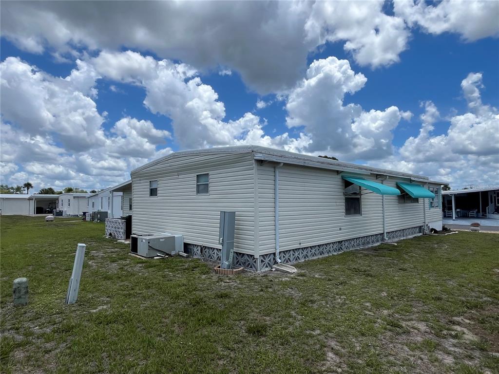 A side view of a light-colored mobile home with metal awnings and a grassy yard — 824 TRENTO, VENICE, FL