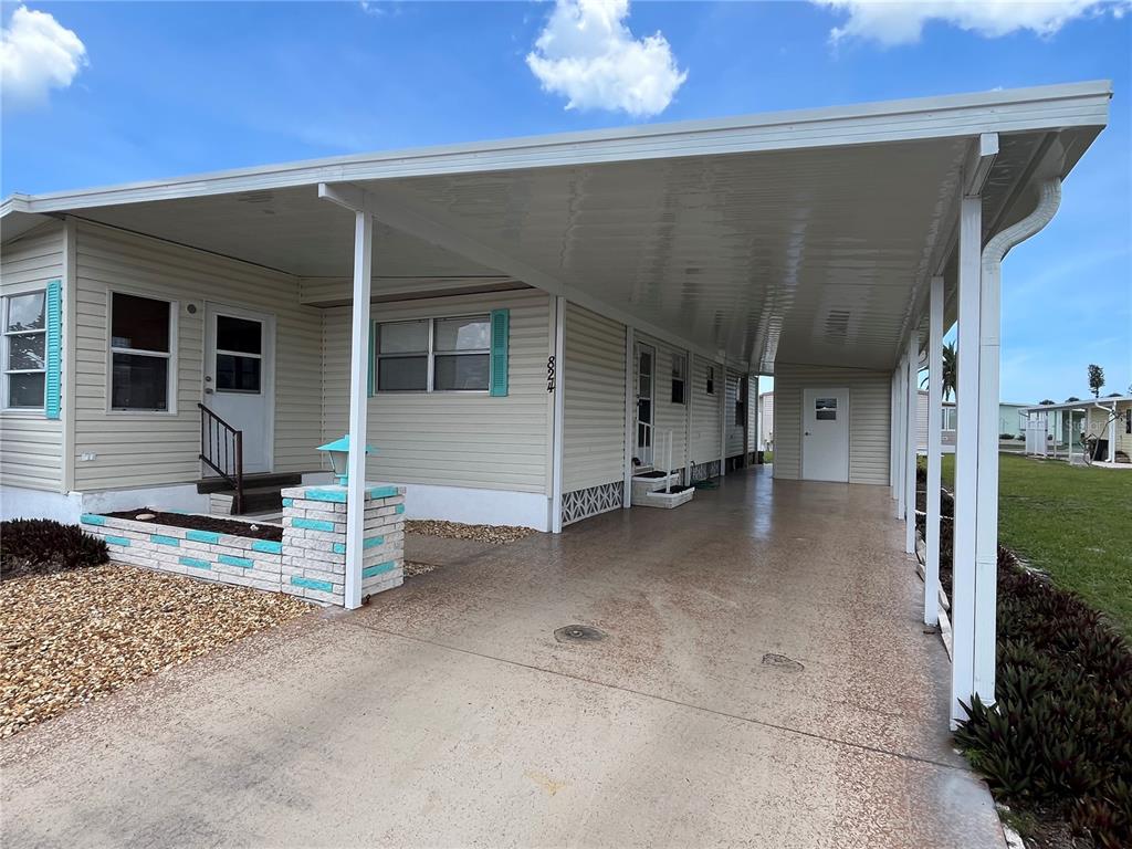 A single-story manufactured home features light siding, a large carport, and a small brick planter — 824 TRENTO, VENICE, FL