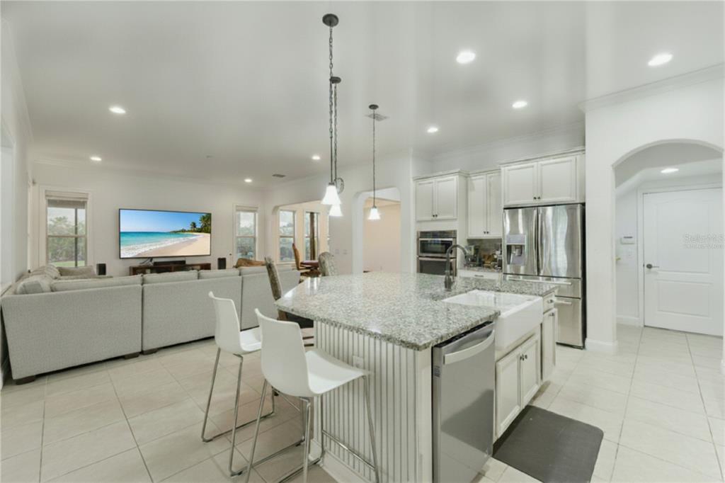 A kitchen with a granite-topped island and white cabinetry opens into a living room area — 6752 TRELLIS VINE LOOP, WINDERMERE, FL