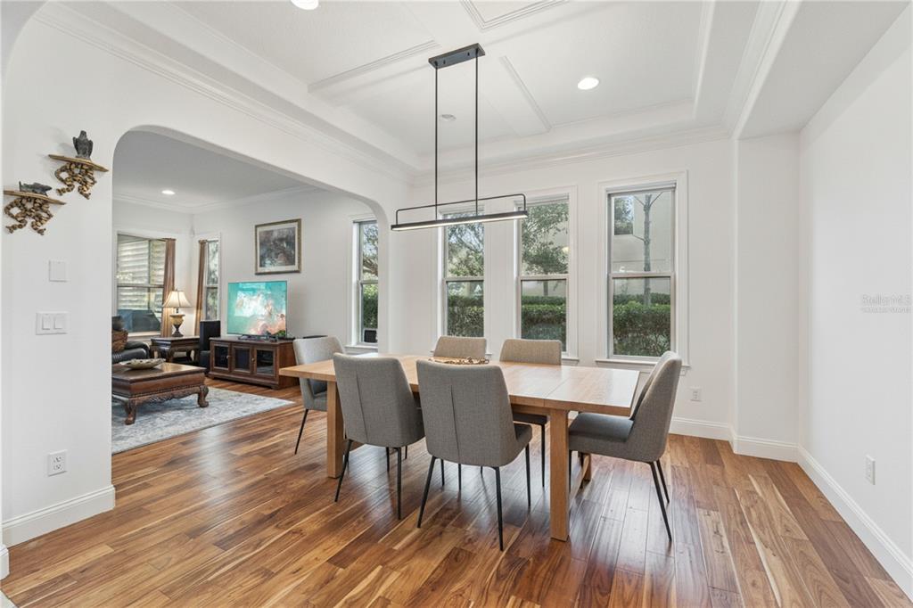 A dining room with a wooden table, gray chairs, and hardwood floors opens to a living area — 6752 TRELLIS VINE LOOP, WINDERMERE, FL