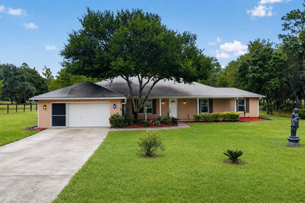 A single-story house with a tan exterior, a two-car garage, and a large shade tree — 389 SW BIG TREE ROAD, DUNNELLON, FL