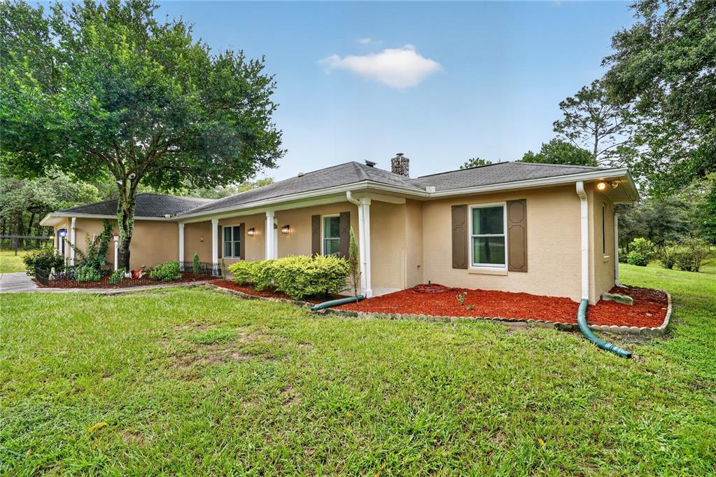 A tan, single-story ranch-style house with a covered porch, brown shutters, and red mulch landscaping — 389 SW BIG TREE ROAD, DUNNELLON, FL