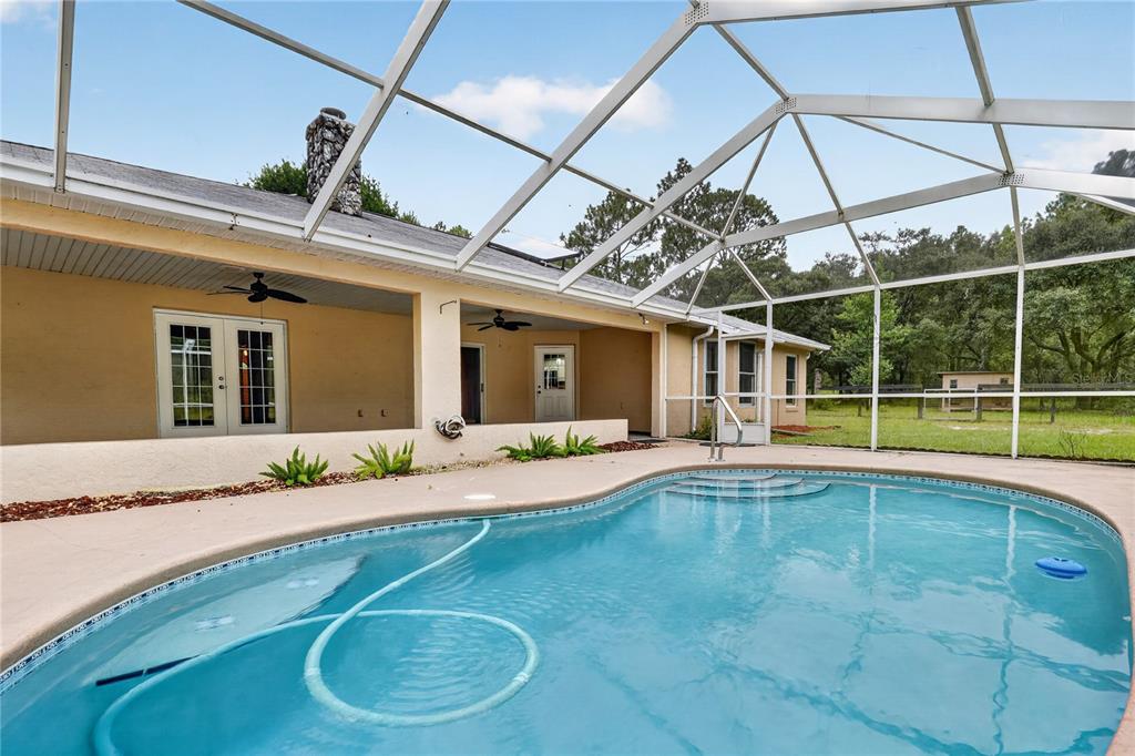 A swimming pool sits on a patio enclosed by a screened lanai behind a house — 389 SW BIG TREE ROAD, DUNNELLON, FL