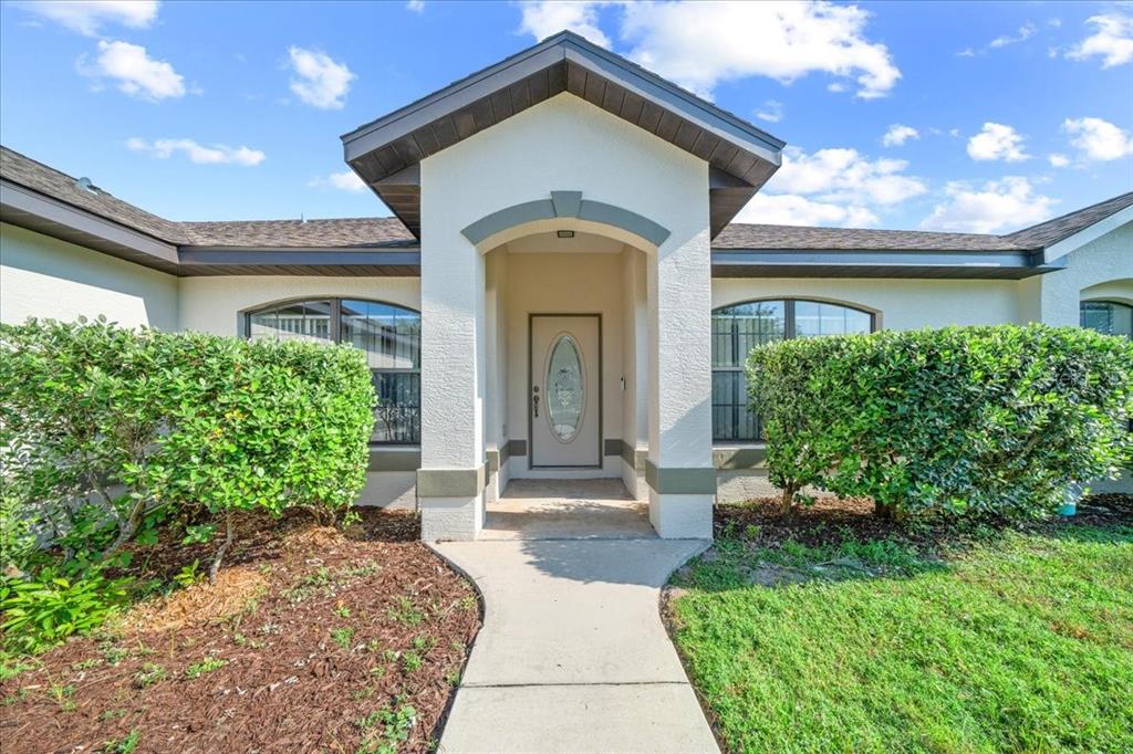 The front exterior of a house features a covered entryway, a glass-paneled door, and landscaping — 5659 SW 89TH PLACE, OCALA, FL