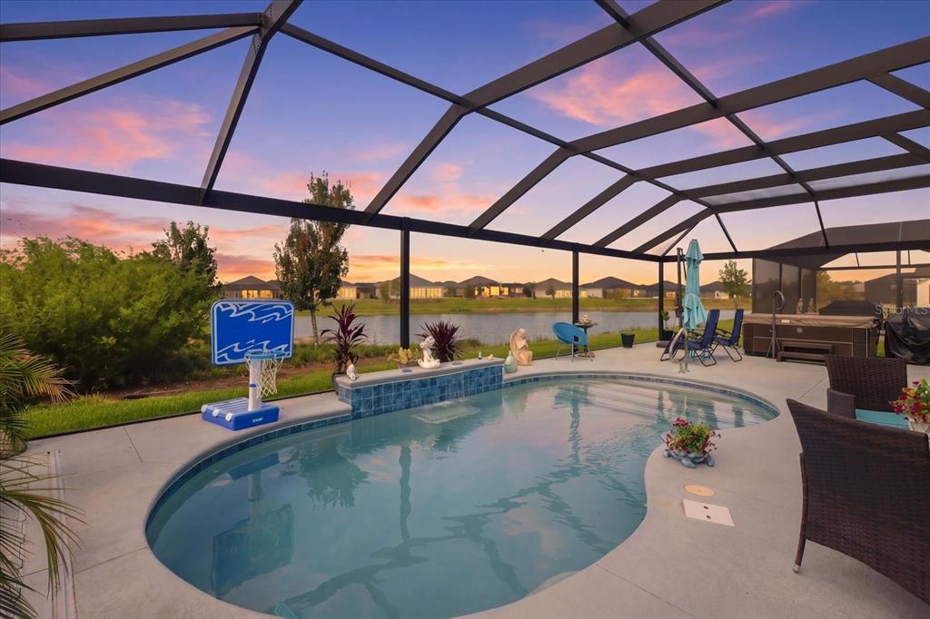 A screened-in patio features a swimming pool, a basketball hoop, and a view of a lake — 7634 FRANK DIPIETRO DR DRIVE, THE VILLAGES, FL