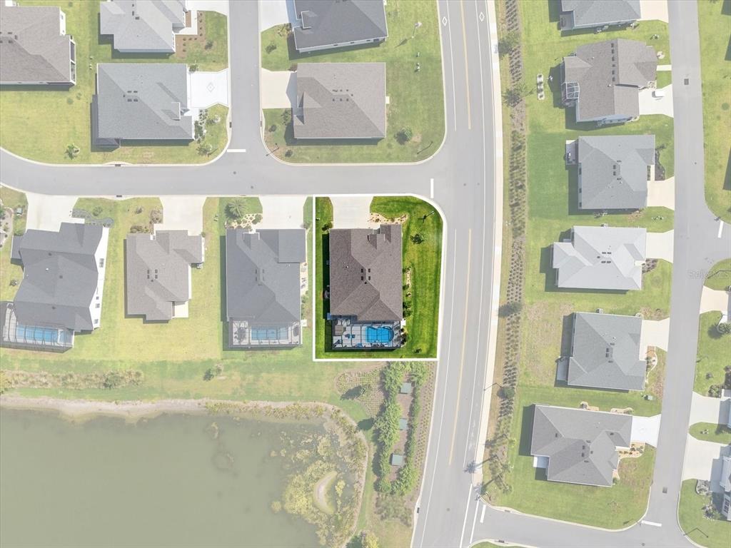 This aerial view shows a residential house with a swimming pool on a corner lot — 7634 FRANK DIPIETRO DR DRIVE, THE VILLAGES, FL
