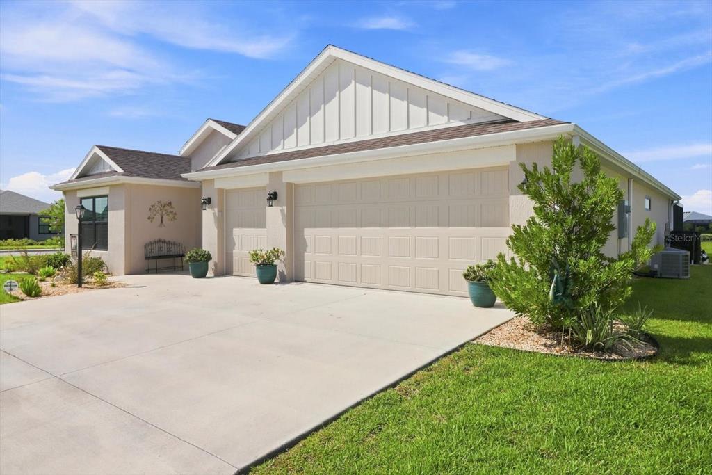A beige house with a three-car garage, board-and-batten siding, and a concrete driveway — 7634 FRANK DIPIETRO DR DRIVE, THE VILLAGES, FL