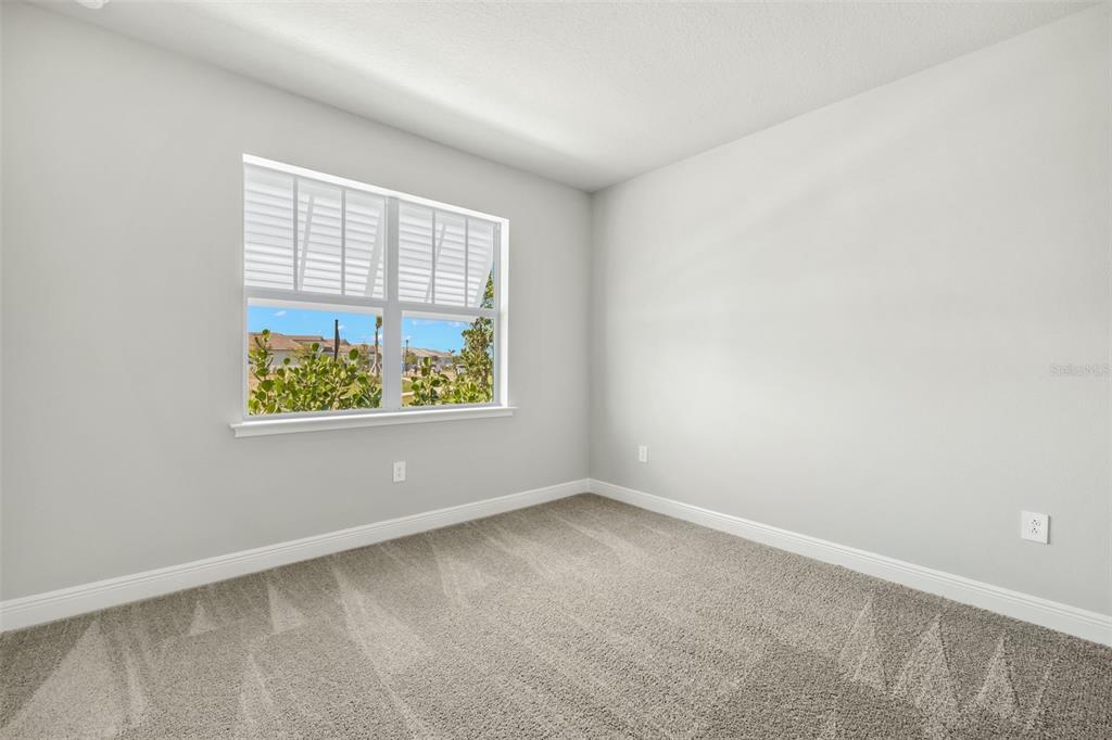 An empty bedroom features light gray walls, beige carpet, and a window overlooking a neighborhood — 18311 CHROMATA DRIVE, VENICE, FL