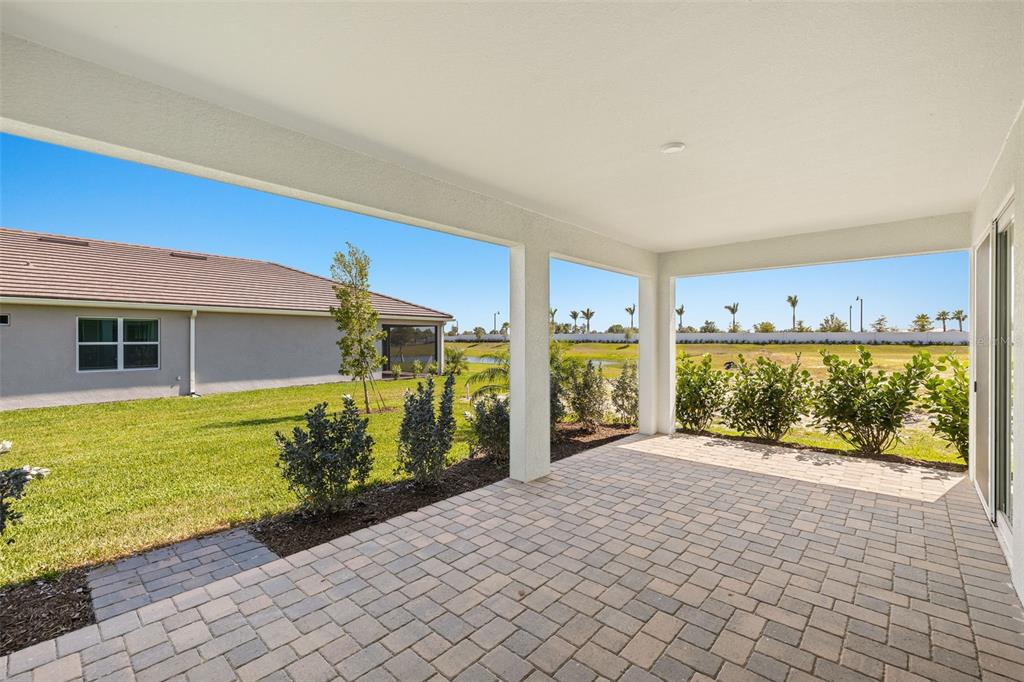A covered patio with paver flooring overlooks a grassy backyard and a neighboring house — 18311 CHROMATA DRIVE, VENICE, FL