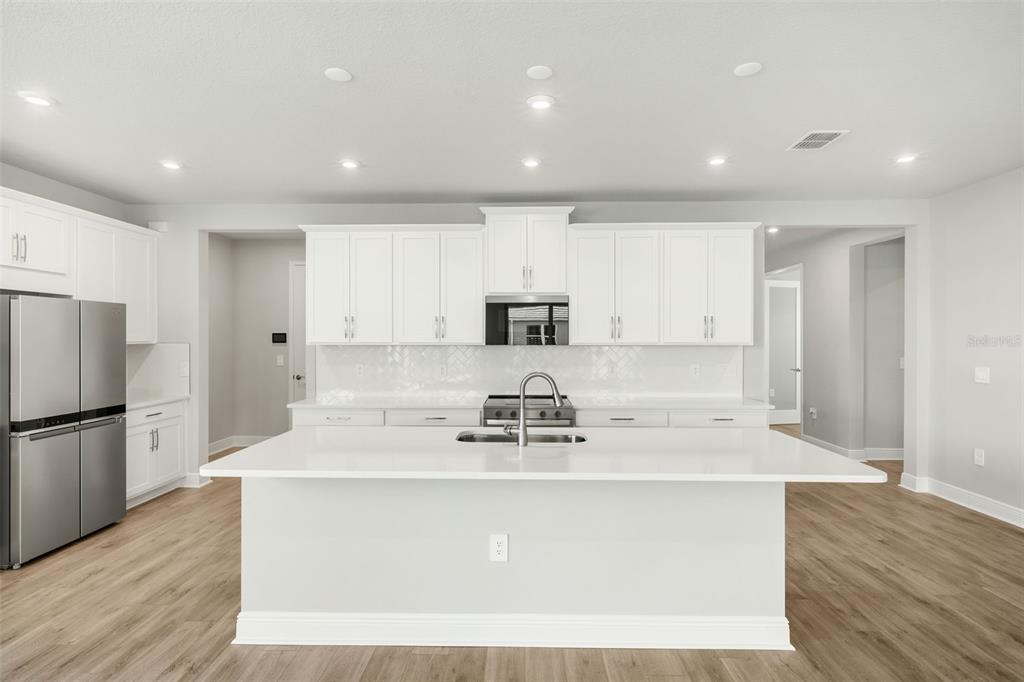 A modern kitchen features white cabinetry, a large central island, and light wood-look flooring — 18311 CHROMATA DRIVE, VENICE, FL
