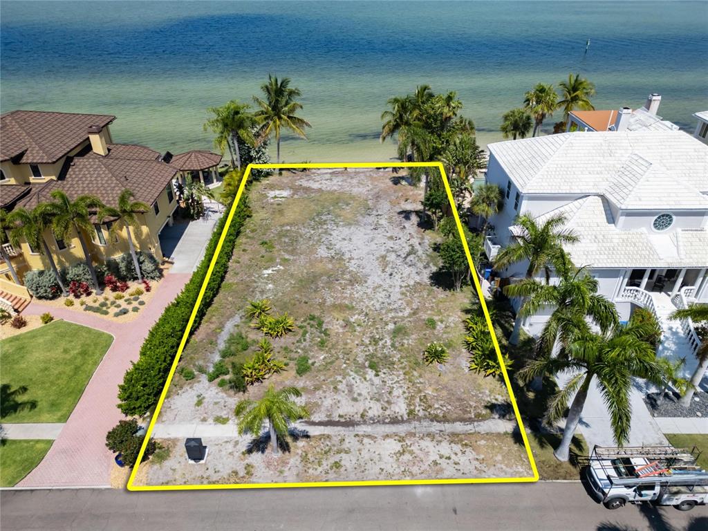 An aerial view shows a vacant, rectangular waterfront lot outlined in yellow between two houses — 1013 SYMPHONY ISLES BOULEVARD, APOLLO BEACH, FL