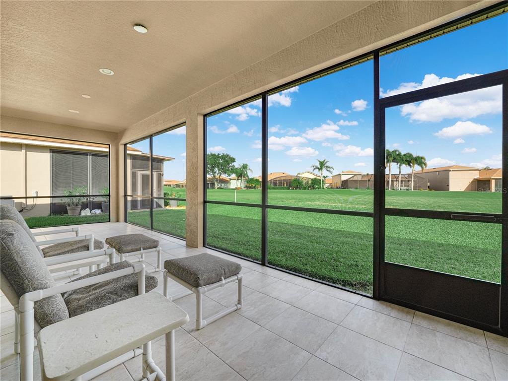 A tiled, screened-in patio overlooks a grassy lawn and neighboring houses under a blue sky — 5197 PEBBLE BEACH BOULEVARD, WINTER HAVEN, FL