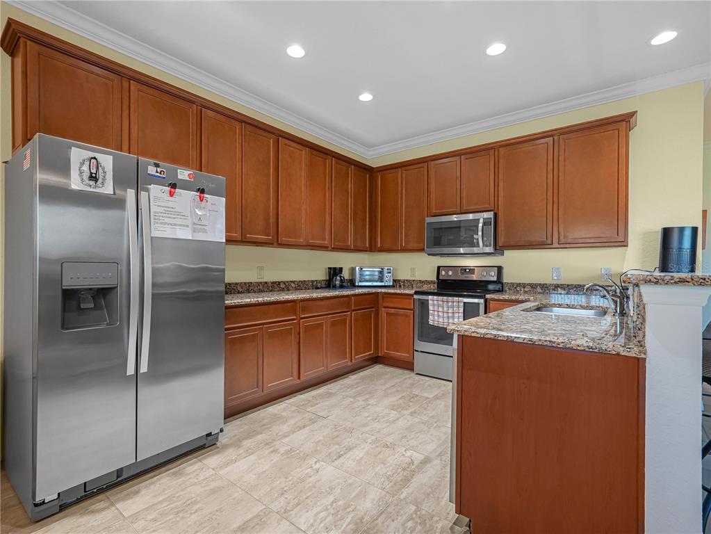 A kitchen features wood cabinets, granite countertops, stainless steel appliances, and light tile flooring — 5197 PEBBLE BEACH BOULEVARD, WINTER HAVEN, FL