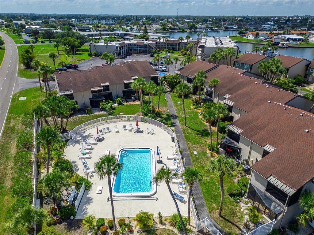 An aerial view shows a swimming pool surrounded by palm trees and multi-story apartment buildings — 1028 APOLLO BEACH BOULEVARD UNIT 104, APOLLO BEACH, FL